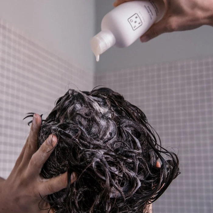 Close-up van nat haar met shampoo ingemasseerd, witte fles shampoo die wordt toegepast in badkamer met tegelwand