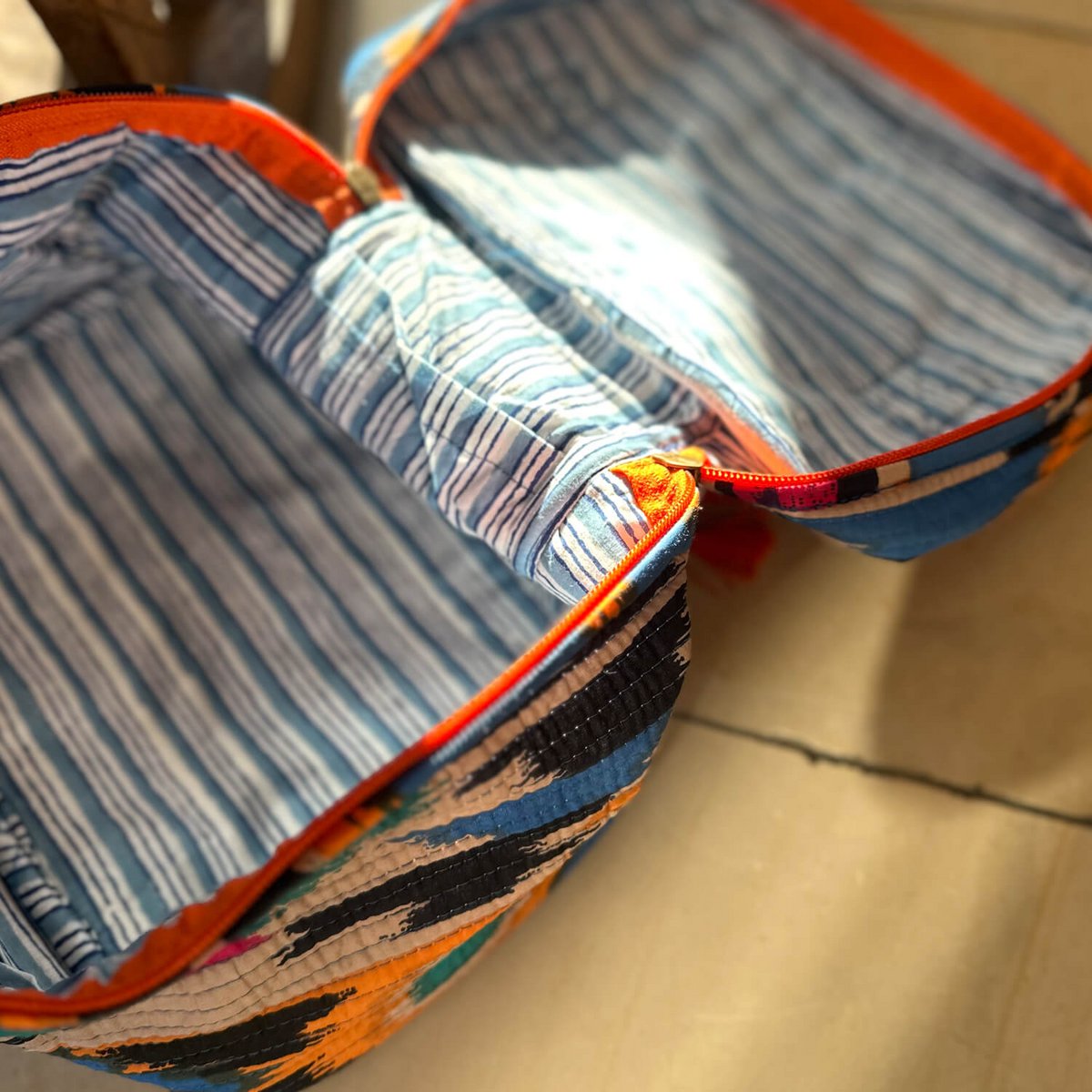 Opengeklapte kleurrijke gestreepte quilt tas met oranje rits op een tegelvloer