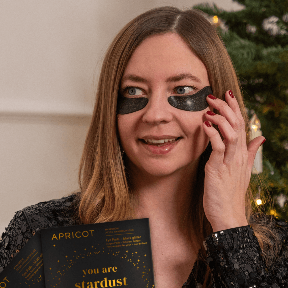 Vrouw met zwarte glinsterende eye pads van Apricot verzorgt haar huid bij kerstboom