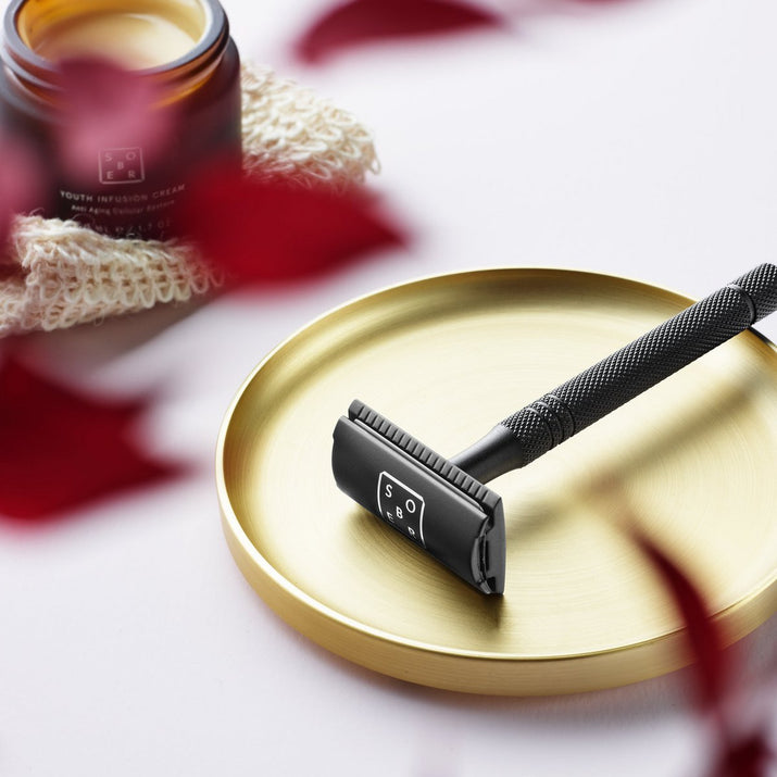 Matte zwarte veiligheidsscheermes op gouden schaal met gezichtscrème op gebreide doek