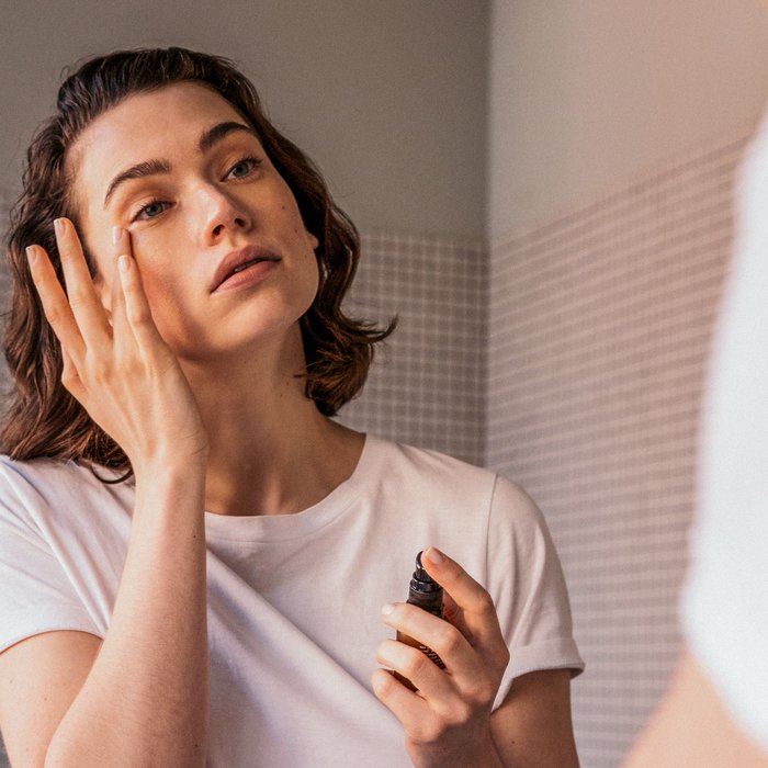 Vrouw brengt gezichtsolie aan in badkamer met witte tegelwand en wit T-shirt
