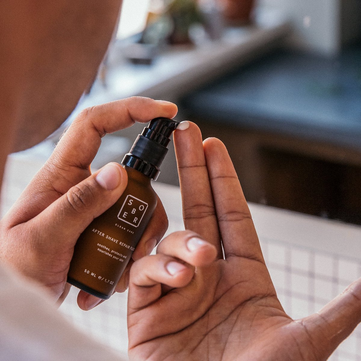 Hand met Sobr after shave repair serum flacon en pompje, scheercrème in dosering op vinger