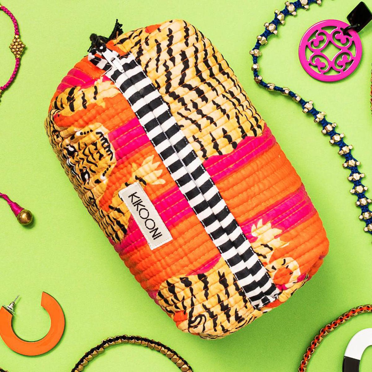 Felgekleurde make-uptas met tijgerprint en zwart-witte rits, omringd door sieraden op groene achtergrond