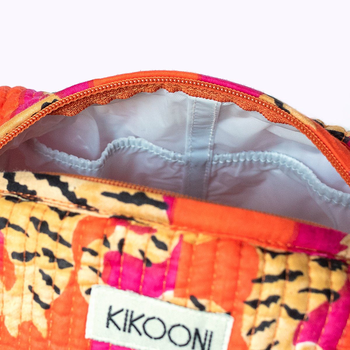 Close-up binnenkant kleurrijke bloemmotief make-uptasje met KIKOONI label en oranje rits