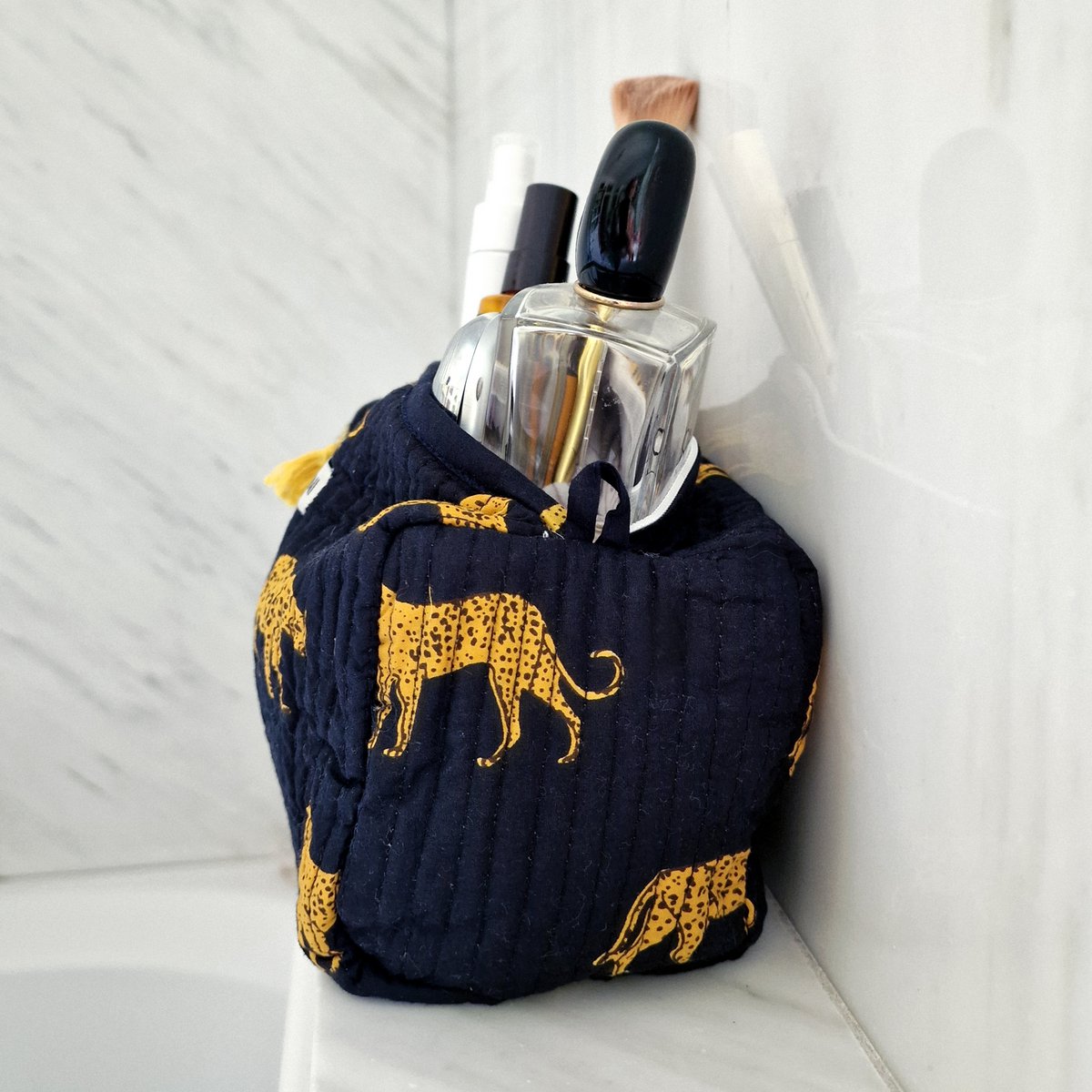 Donkerblauw quiltet make-uptasje met gele luipaardprint en cosmetica in witte badkamerhoek
