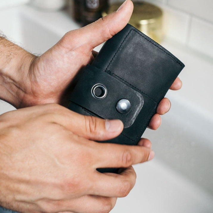 Close-up van handen die een zwarte leren herenportemonnee met metalen drukknop vasthouden