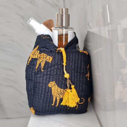Donkerblauw gestikt cosmeticatasje met gele luipaardprint en kwastjes, gevuld met verzorgingsproducten