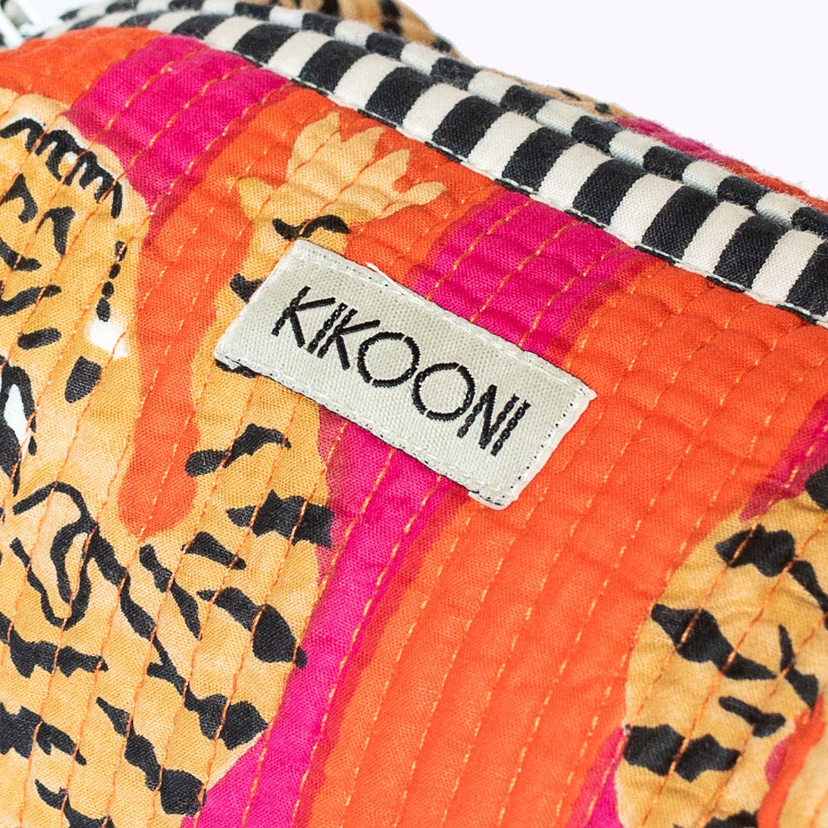 Close-up van kleurrijk quilted textiel met label 'Kikooni' en zwart-witte gestreepte rand
