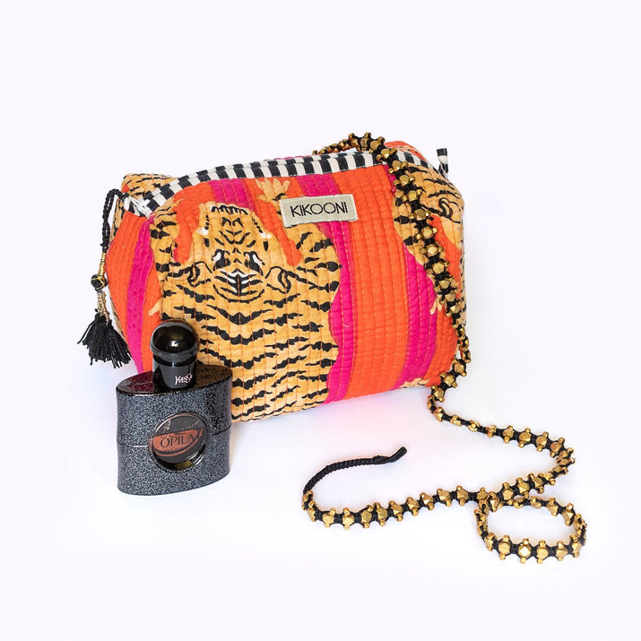 KIKONI kleurrijke tas met tijgerprint en ketting, naast zwarte Yves Saint Laurent Black Opium parfumfles