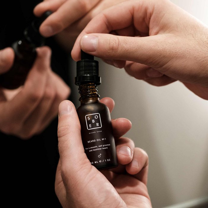 Hand die Sober Beard Oil fles vasthoudt met druppelaar voor baardverzorging