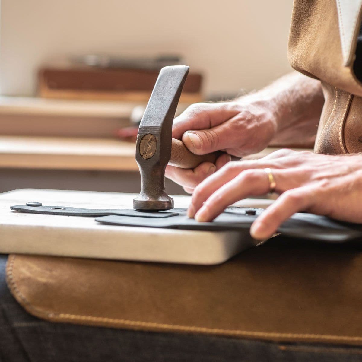 Handen van een ambachtsman die een houten hamer gebruikt om zwart leer te bewerken op een werkbank