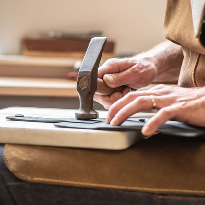 Handen van een ambachtsman die een houten hamer gebruikt om zwart leer te bewerken op een werkbank