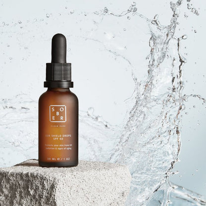 SOBER Sun Shield Drops SPF 50 in een bruine fles met pipet, water splash achtergrond