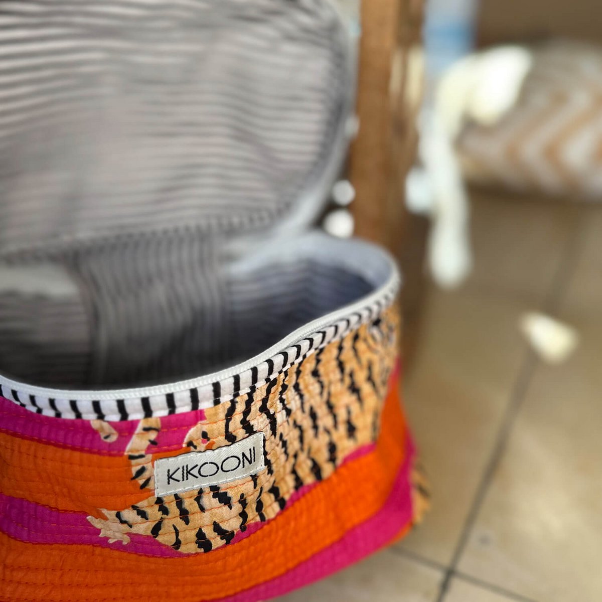 Kleurrijke opbergmand met label KIKOONI, geopend, met oranje, roze en tijgerprint stof, gestreept interieur