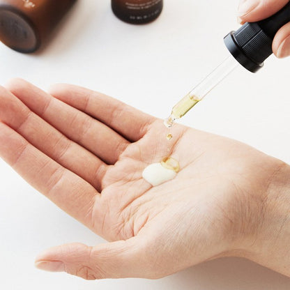 Hand met druppelaar die olie en crème voor huidverzorging toont, witte achtergrond