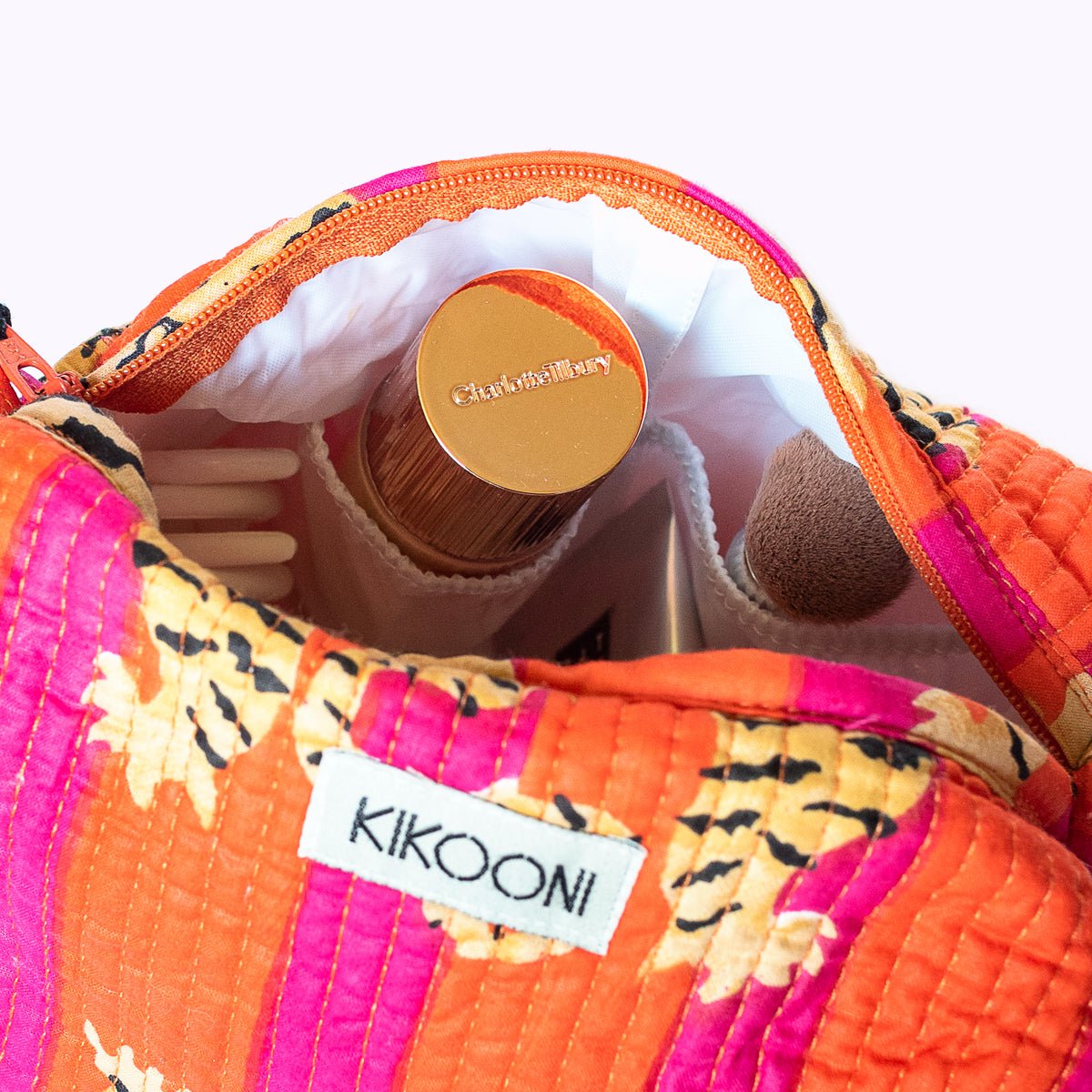 Oranje en roze cosmetische tas met Charlotte Tilbury make-up en kwast